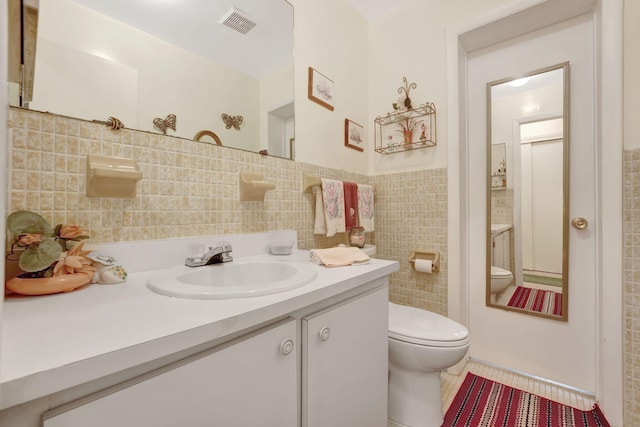 bathroom with toilet, vanity, tile patterned floors, and tile walls