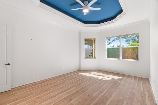 unfurnished room featuring a tray ceiling, ceiling fan, crown molding, and light wood-type flooring