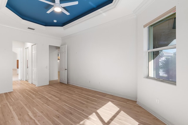 empty room with light hardwood / wood-style flooring, a raised ceiling, ceiling fan, and crown molding