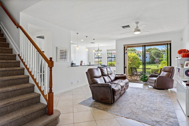 tiled living room featuring ceiling fan with notable chandelier and a textured ceiling