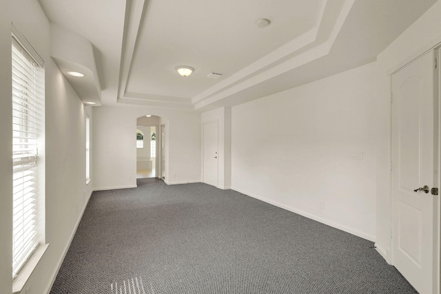 unfurnished room featuring a raised ceiling, dark carpet, and plenty of natural light