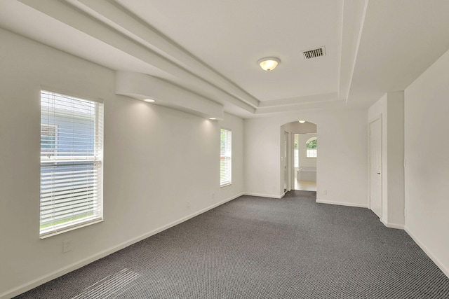 spare room featuring a tray ceiling and dark colored carpet