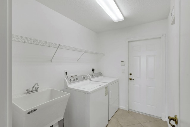 laundry area with sink, washer and dryer, light tile patterned floors, and a textured ceiling