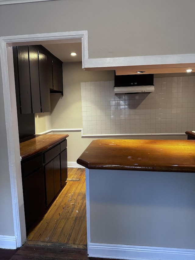 130 NE 4th Ave, Boynton Beach, FL 33435 - kitchen with hardwood / wood-style floors, dark cabinetry, baseboards, backsplash, and range hood
