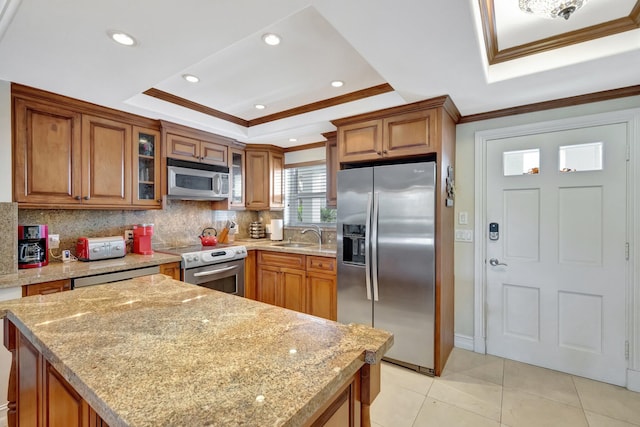 kitchen with stainless steel appliances, tasteful backsplash, a tray ceiling, light tile patterned flooring, and ornamental molding