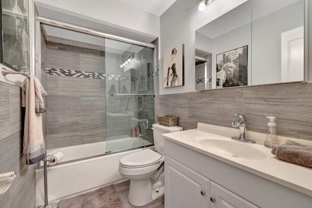 full bathroom with vanity, toilet, tile walls, and bath / shower combo with glass door