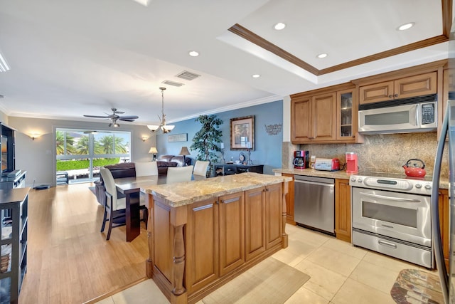 kitchen with light stone counters, appliances with stainless steel finishes, decorative light fixtures, a kitchen island, and ornamental molding