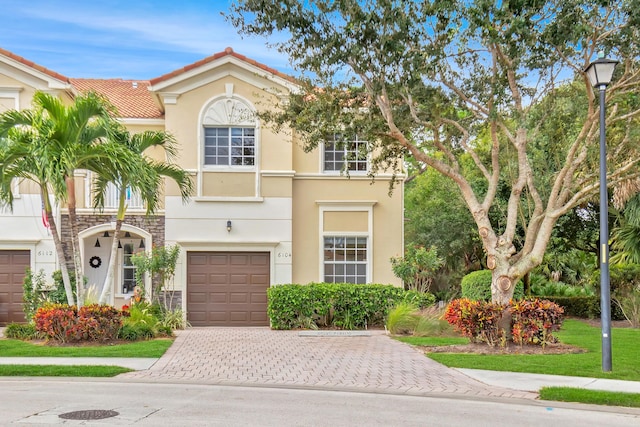 view of front of home featuring an attached garage, stone siding, driveway, stucco siding, and a tiled roof