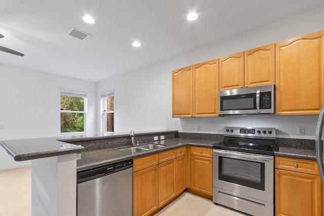 kitchen with a sink, a peninsula, dark stone counters, light tile patterned floors, and appliances with stainless steel finishes