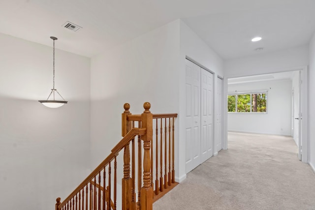 hallway with baseboards, an upstairs landing, visible vents, and light colored carpet