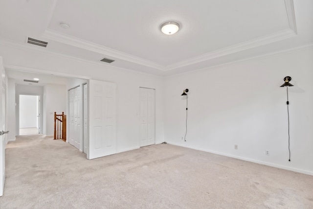 empty room with a tray ceiling, light colored carpet, and visible vents