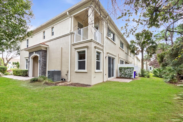 back of property featuring a balcony, a lawn, central AC, stucco siding, and stone siding