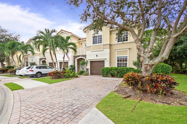 mediterranean / spanish house featuring a balcony, stucco siding, a garage, and decorative driveway