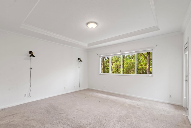 empty room featuring a tray ceiling, light colored carpet, ornamental molding, and baseboards