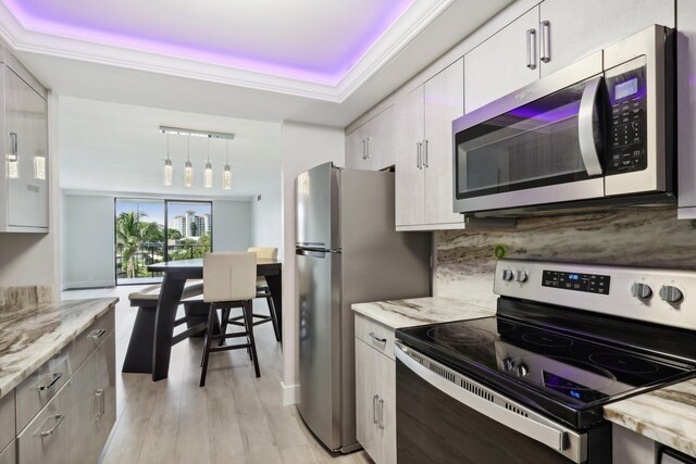 kitchen with appliances with stainless steel finishes, pendant lighting, tasteful backsplash, white cabinets, and light wood-type flooring