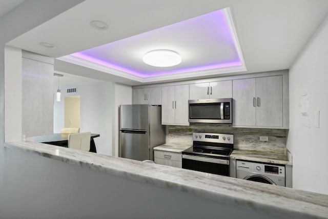 kitchen featuring backsplash, hanging light fixtures, stainless steel appliances, a tray ceiling, and washer / dryer