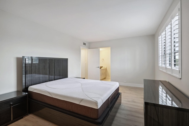 bedroom featuring connected bathroom and light hardwood / wood-style floors