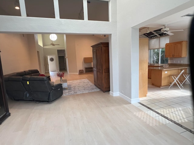 living room featuring sink, light hardwood / wood-style flooring, a towering ceiling, and ceiling fan