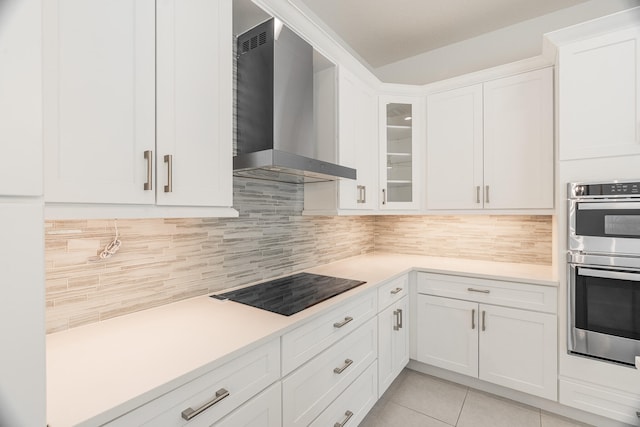 kitchen with stainless steel double oven, white cabinetry, backsplash, black electric cooktop, and wall chimney exhaust hood