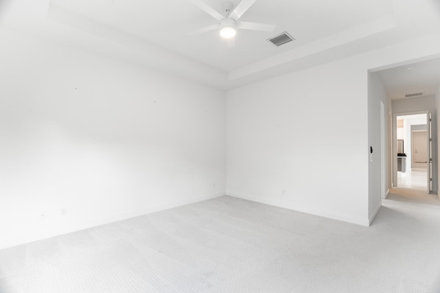 empty room featuring light carpet, ceiling fan, and a raised ceiling