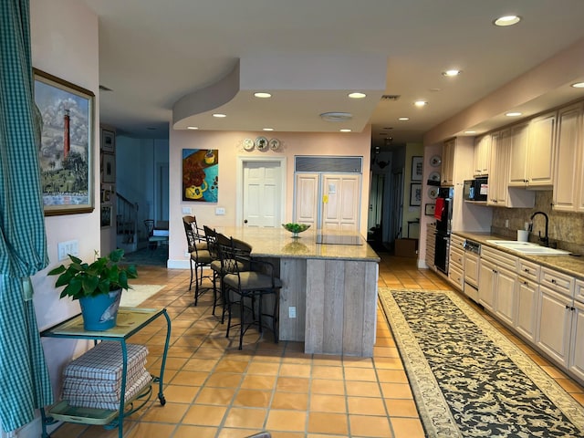 kitchen with light stone countertops, a center island, tasteful backsplash, sink, and a breakfast bar area