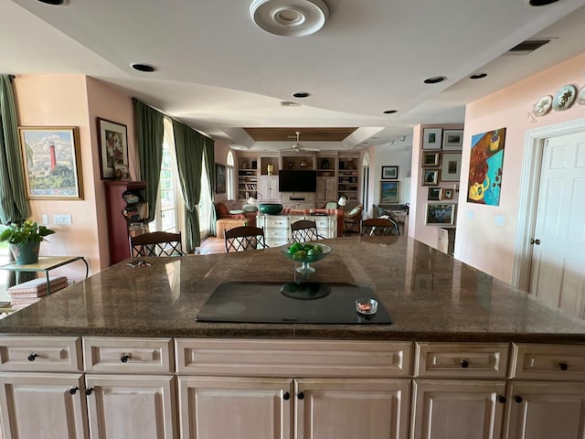 kitchen with black electric stovetop, a center island, a raised ceiling, built in features, and dark stone counters