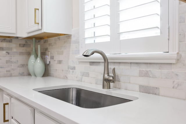 interior details with sink, white cabinetry, and tasteful backsplash