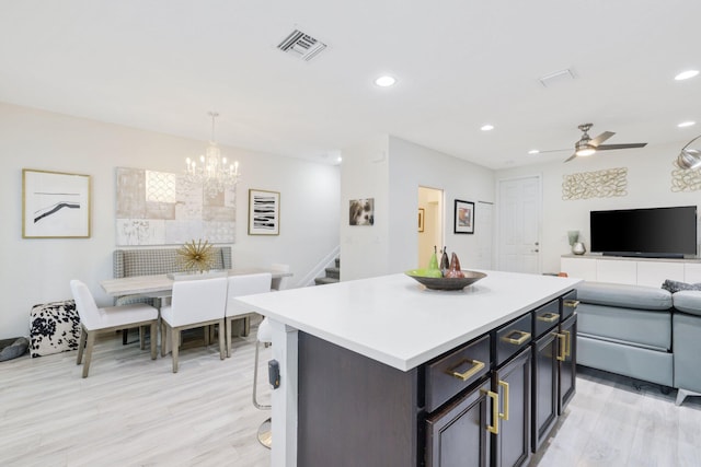 kitchen with a kitchen island, a breakfast bar, light hardwood / wood-style flooring, ceiling fan with notable chandelier, and pendant lighting