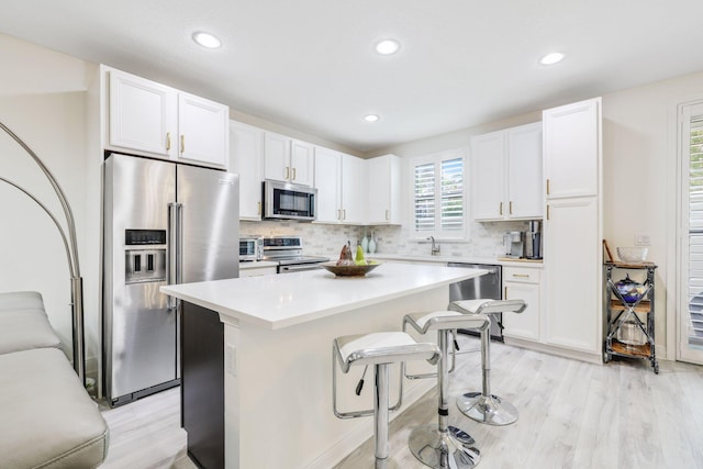 kitchen with backsplash, appliances with stainless steel finishes, white cabinetry, light hardwood / wood-style floors, and a center island