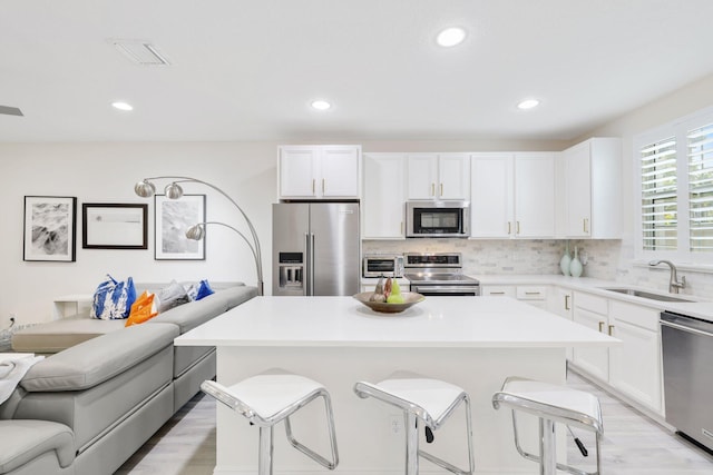 kitchen featuring sink, a center island, stainless steel appliances, white cabinets, and a breakfast bar