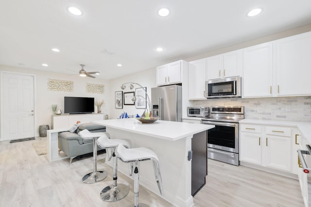 kitchen with a breakfast bar area, appliances with stainless steel finishes, white cabinetry, and light hardwood / wood-style floors