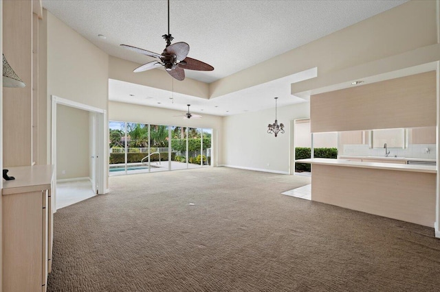 unfurnished living room featuring carpet, a textured ceiling, ceiling fan with notable chandelier, a towering ceiling, and sink