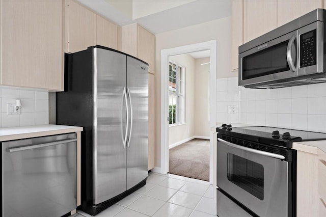 kitchen featuring light brown cabinetry, appliances with stainless steel finishes, light tile patterned floors, and decorative backsplash