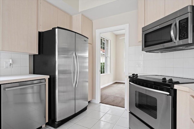 kitchen with backsplash, light brown cabinetry, light countertops, stainless steel appliances, and light tile patterned flooring