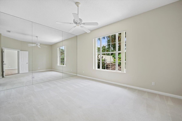 carpeted empty room featuring baseboards, ceiling fan, a textured ceiling, and visible vents