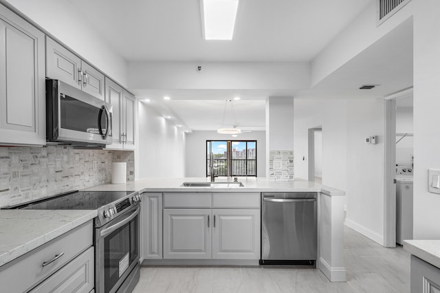 kitchen with gray cabinets, kitchen peninsula, stainless steel appliances, and tasteful backsplash