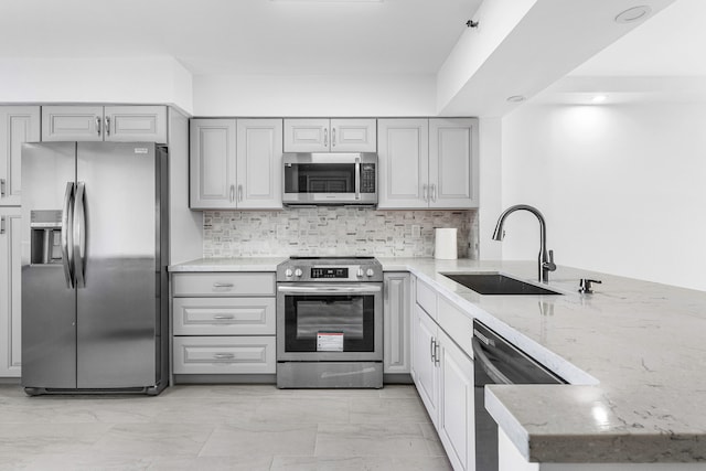 kitchen featuring kitchen peninsula, decorative backsplash, light stone counters, sink, and stainless steel appliances