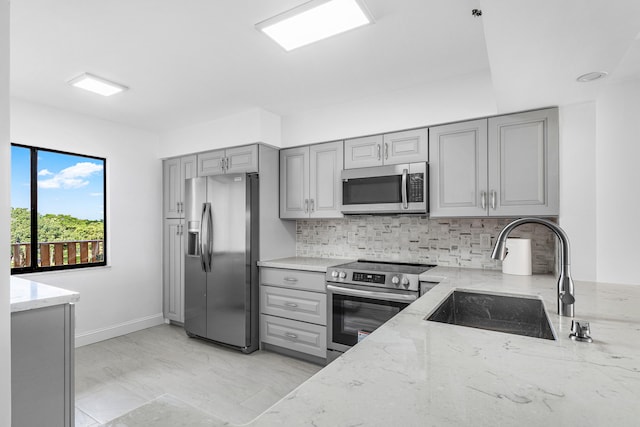 kitchen with decorative backsplash, appliances with stainless steel finishes, light stone countertops, gray cabinets, and sink