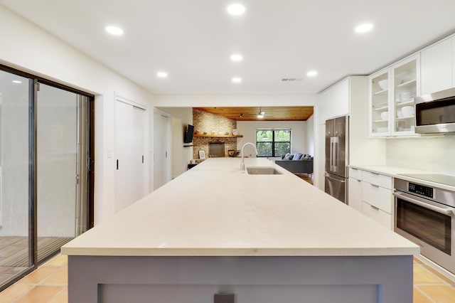 kitchen with sink, stainless steel appliances, white cabinetry, and a kitchen island with sink