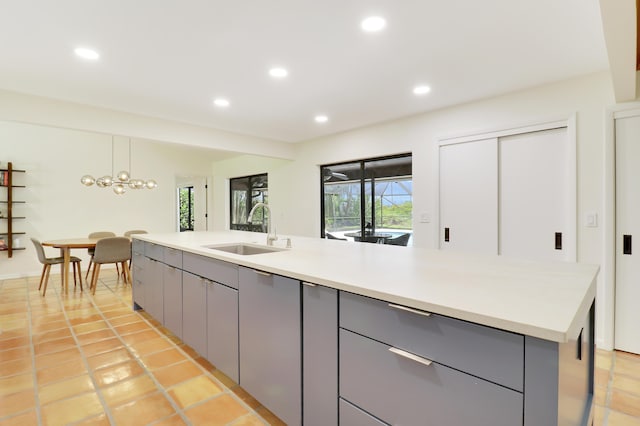 kitchen featuring a kitchen island with sink, gray cabinetry, hanging light fixtures, a notable chandelier, and sink