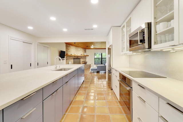 kitchen with stainless steel appliances, gray cabinets, white cabinetry, a fireplace, and sink