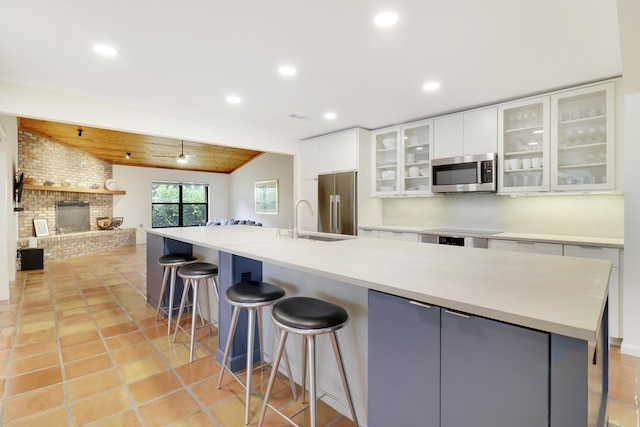 kitchen featuring vaulted ceiling, white cabinetry, a fireplace, appliances with stainless steel finishes, and sink