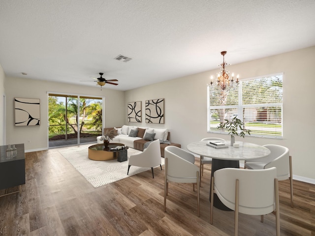 dining room with ceiling fan with notable chandelier, wood-type flooring, and a textured ceiling