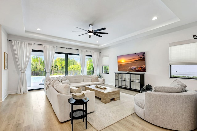 living room featuring light wood-type flooring, a raised ceiling, and ceiling fan