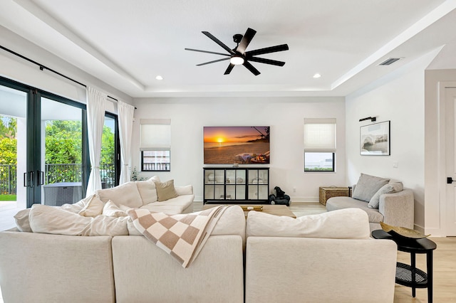 living room with a raised ceiling, ceiling fan, and light hardwood / wood-style floors