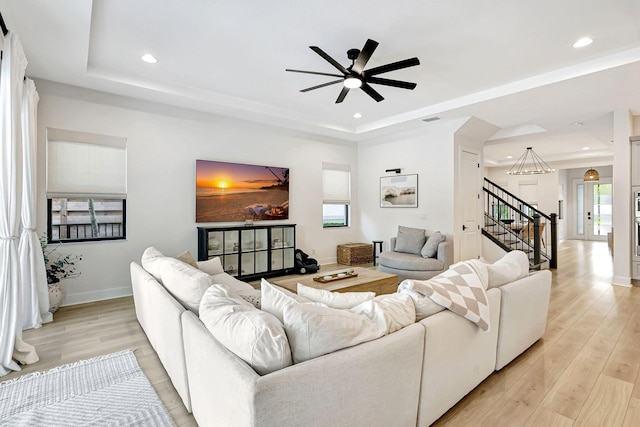 living room featuring a raised ceiling, ceiling fan, and light hardwood / wood-style floors