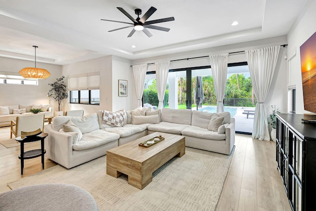 living room with a tray ceiling, ceiling fan, and light wood-type flooring