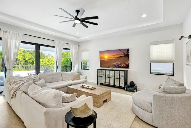 living room with ceiling fan, light hardwood / wood-style floors, french doors, and a tray ceiling