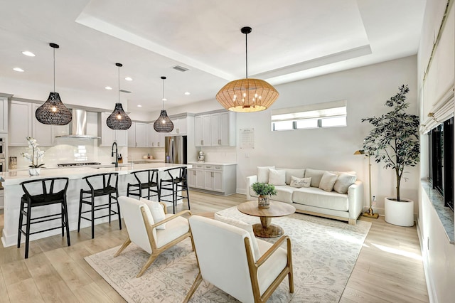 living room featuring a tray ceiling, sink, a chandelier, and light wood-type flooring