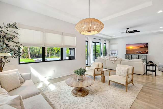 living room with ceiling fan with notable chandelier, light hardwood / wood-style floors, and a raised ceiling